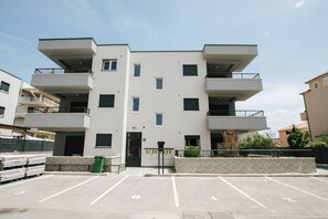 Ein mehrgeschossiges Wohngebäude mit Balkonen, einem Parkplatz und einer kleinen Grünfläche.
