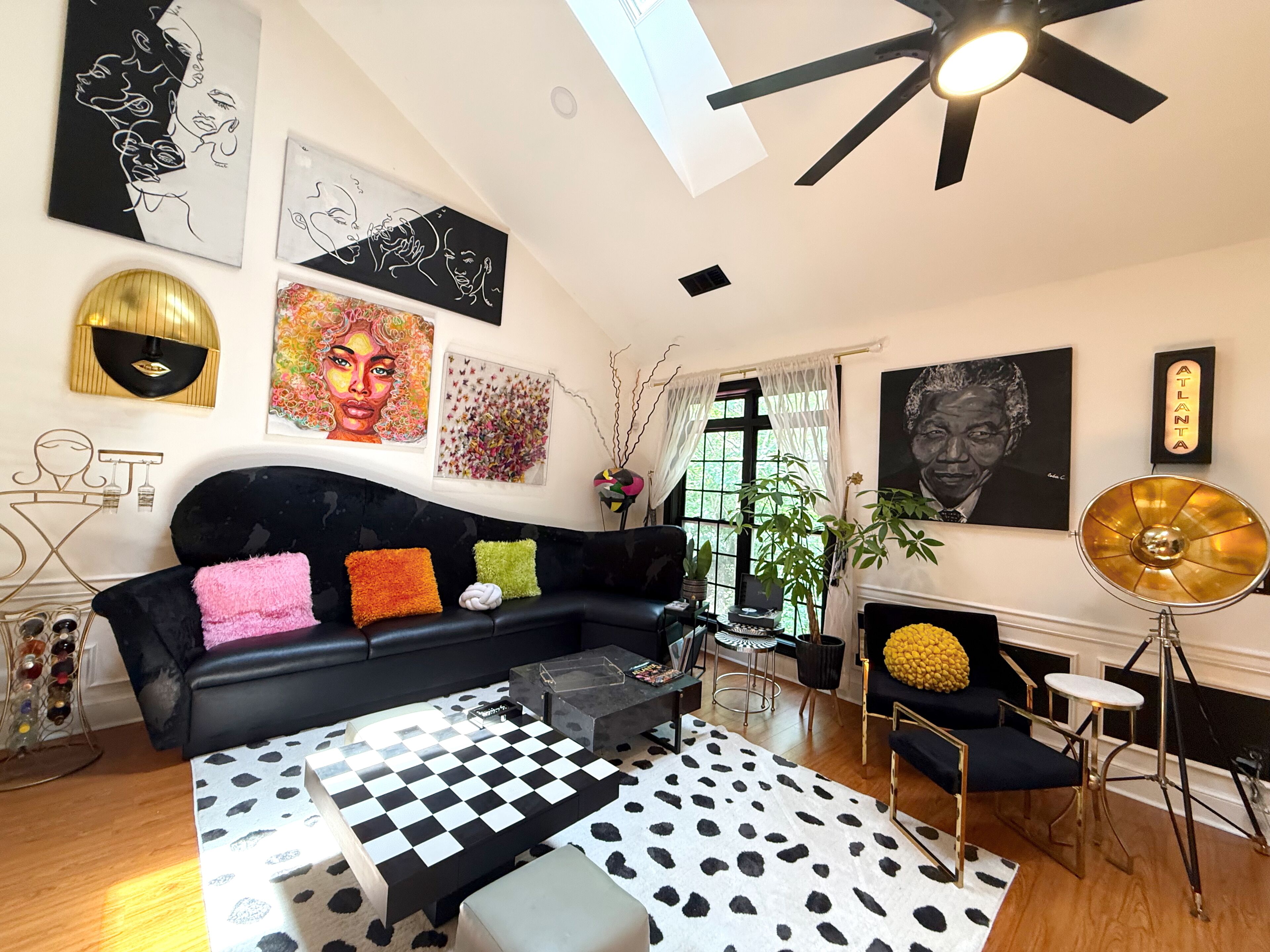 Un salon moderne avec un canapé noir, un tapis à carreaux et diverses œuvres d’art murales.