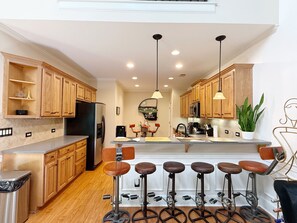 A modern kitchen with wooden cabinets, a black refrigerator, a central island with stools, pendant lighting, and a potted plant. - Luxury Atlanta Townhome- Near Airport- 15 Min to Mercedes-Benz Stadium (Atlanta)