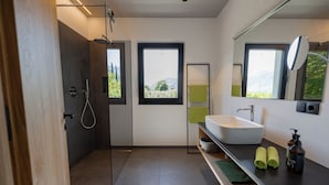 Une salle de bain moderne équipée d’une douche, d’un lavabo, d’un miroir et offrant une vue sur l’extérieur.