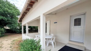 A covered outdoor area with a table and chairs, a door, and a garden with plants and a gravel path. - Beach Wood Green (Dolus-d'Oléron)