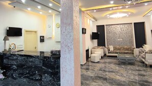 Un vestíbulo moderno con suelo de mármol, un mostrador de recepción, un conjunto de sofás y una pared decorativa.