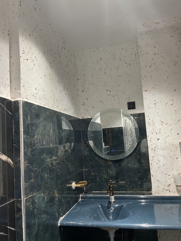A bathroom with a marble sink, a round mirror, and a wall-mounted light fixture.