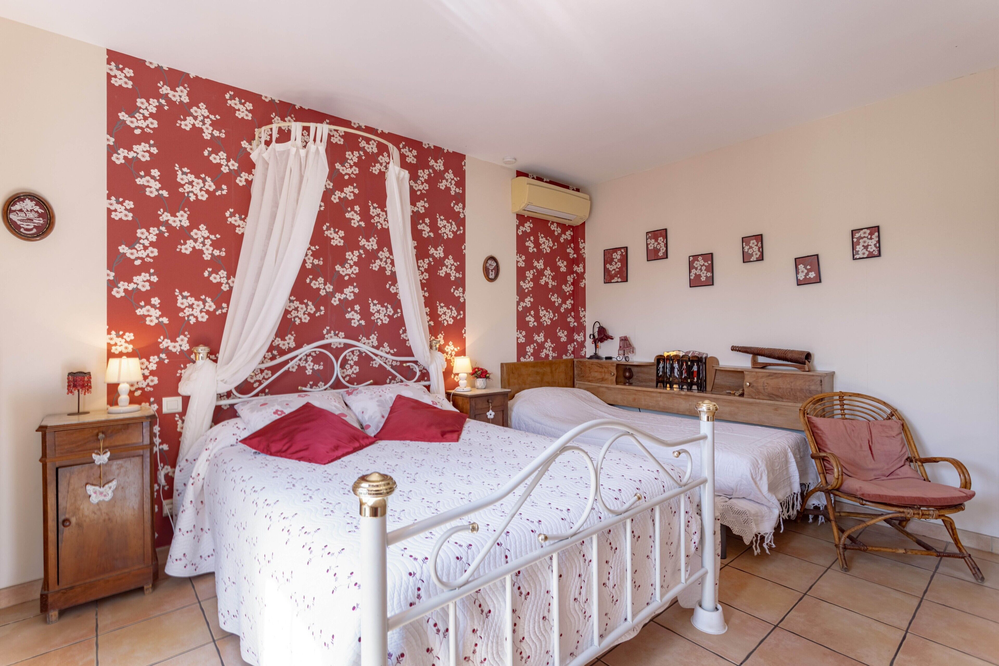 Une chambre à coucher avec un lit à baldaquin, une table de chevet avec une lampe, une commode en bois, une chaise en osier et une coiffeuse avec un miroir.