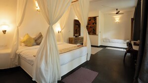 Ein Schlafzimmer mit Himmelbett, Nachttisch, Sessel, Schreibtisch und Wandfernseher.