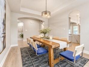 Zona pranzo con tavolo in legno, sedie imbottite blu, un vaso con fiori e una lampada a sospensione.