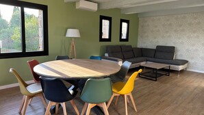 A modern living room with a round wooden table, colorful chairs, a gray sectional sofa, and a patterned wall.