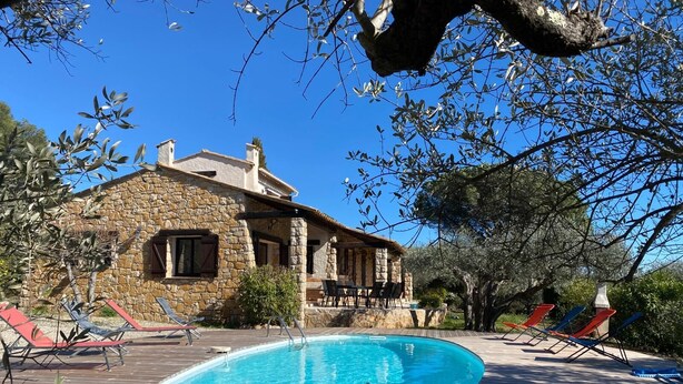 A stone building with a swimming pool, outdoor seating, and surrounding trees.