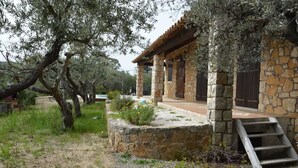 A stone building with a wooden porch, a stone staircase, and olive trees in the background.