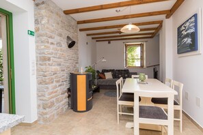 Ein Zimmer mit Steinwand, Kamin, Esstisch mit Stühlen, einer Couch und einem Fenster.