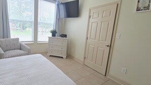 A bedroom with a bed, a chair, a dresser, a door, and a window with blinds.