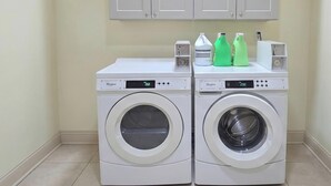 Two white front-loading washing machines with digital displays, placed in a corner with a tiled floor and light-colored walls.