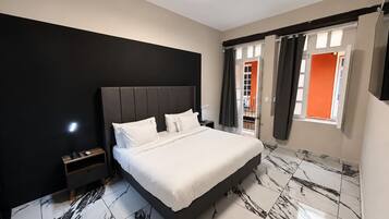 A modern bedroom with a large bed, a nightstand, a ceiling light, and a view of the outside through a window with curtains.