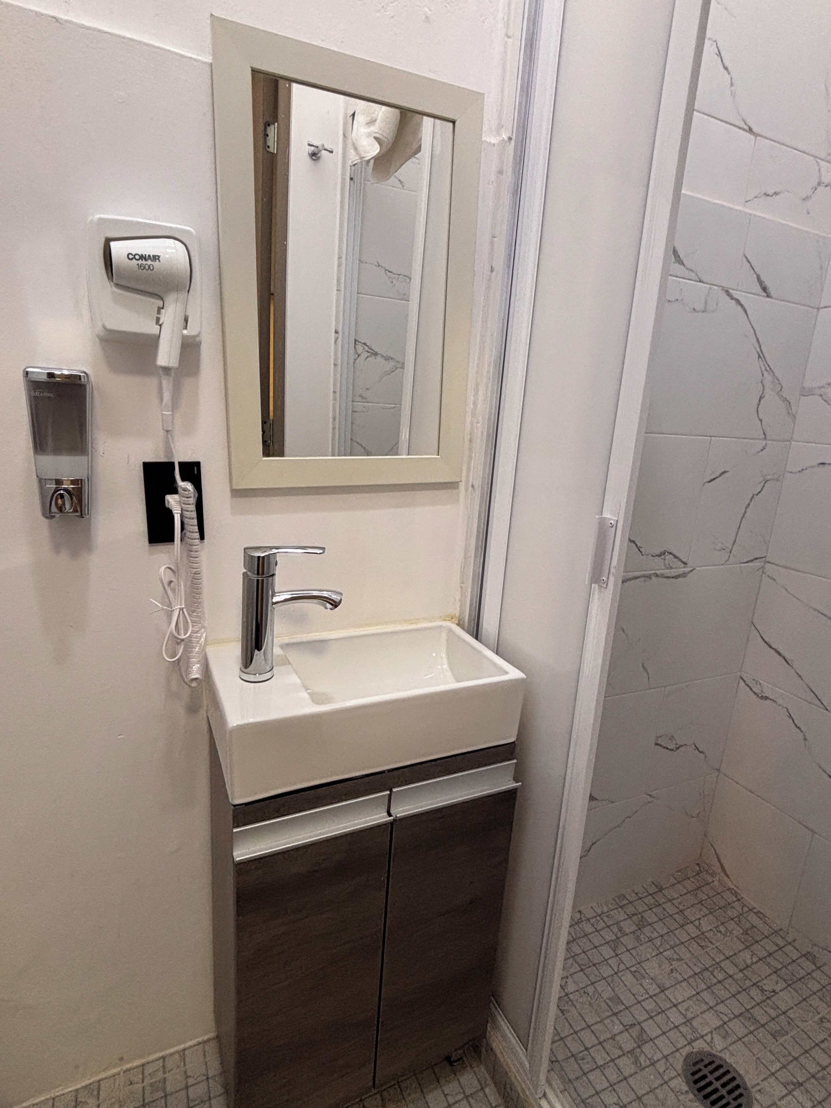 A bathroom with a white sink, a mirror, a hairdryer, and a shower area.