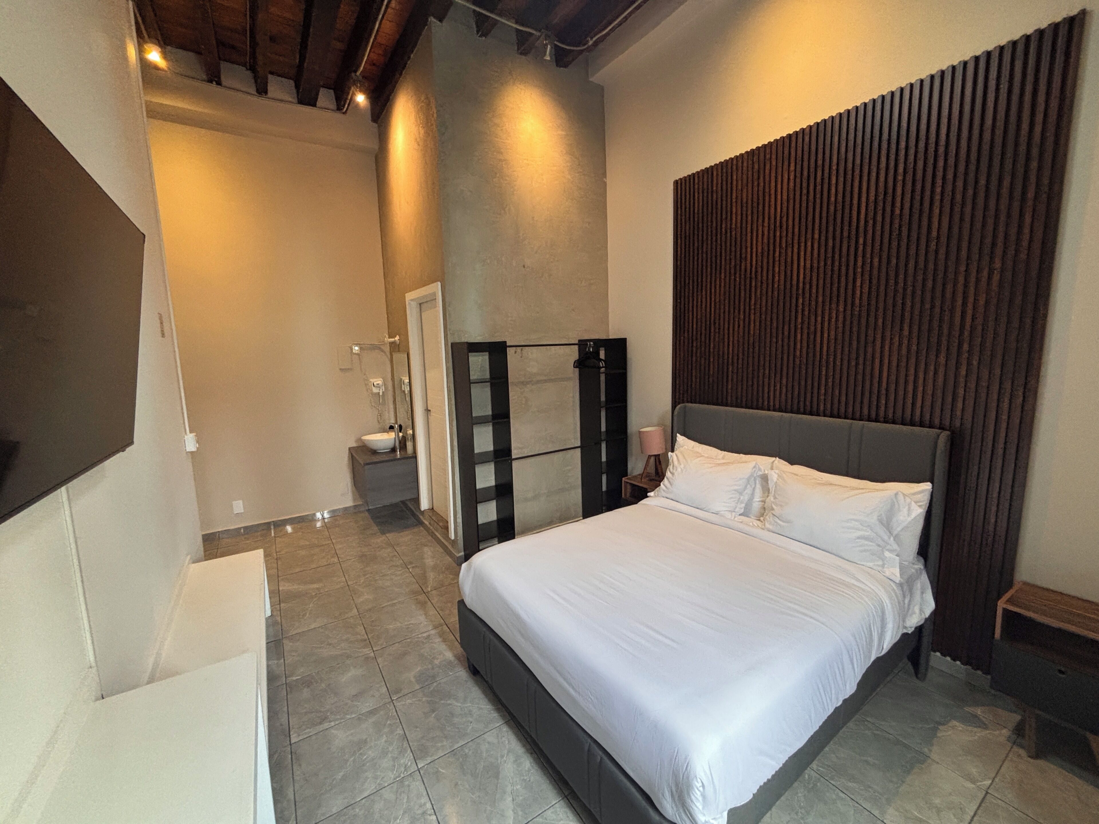 Um quarto moderno com uma cama grande, uma mesa de cabeceira, um espelho e um painel de madeira embutido na parede.
