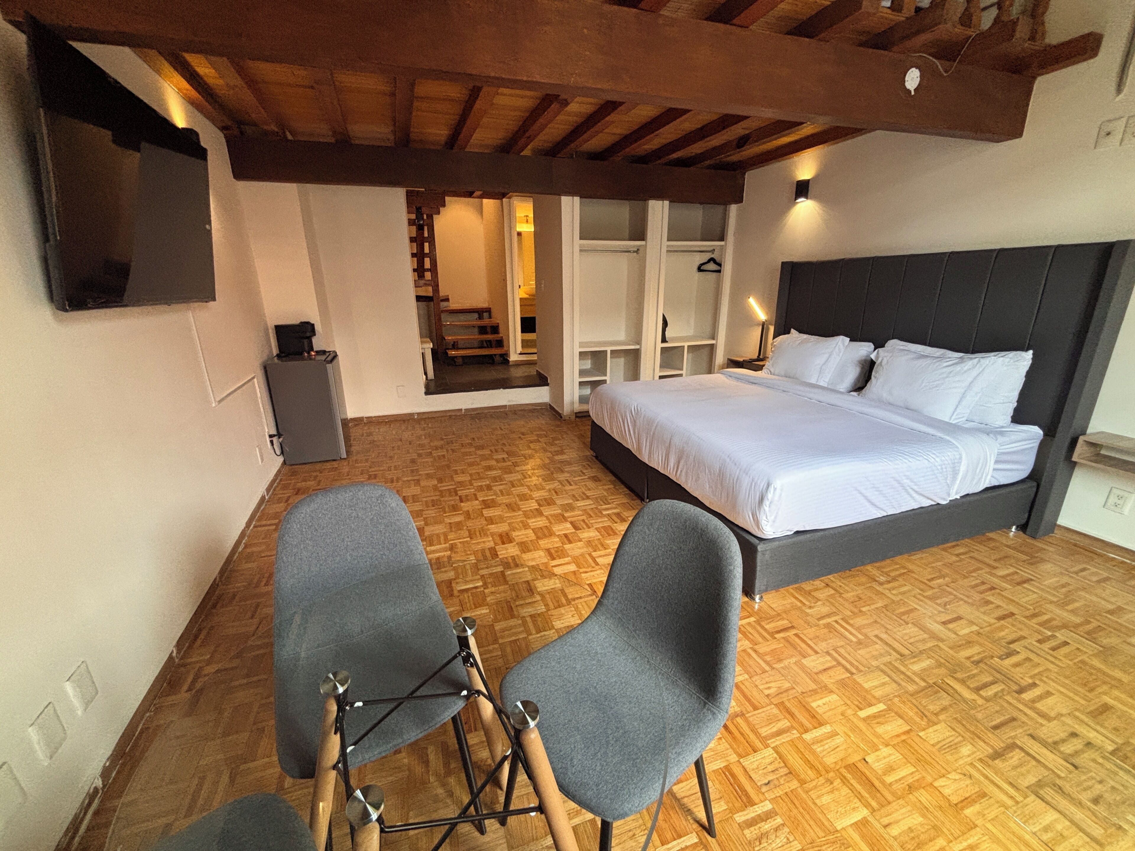 A bedroom with a bed, two chairs, a television, and a staircase leading to an upper level.