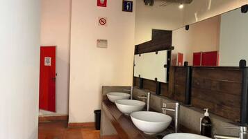 Eine öffentliche Toilette mit vier Waschbecken, einer roten Tür und einem Spiegel mit Holzrahmen.