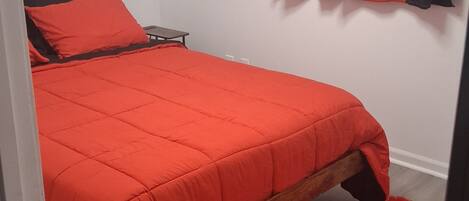 Un dormitorio con cama, una mesita y un tapete rojo.