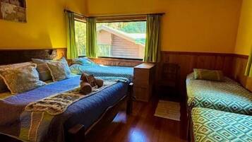 Habitación con dos camas, suelo y techo de madera, una ventana con cortinas y una lámpara colgante.