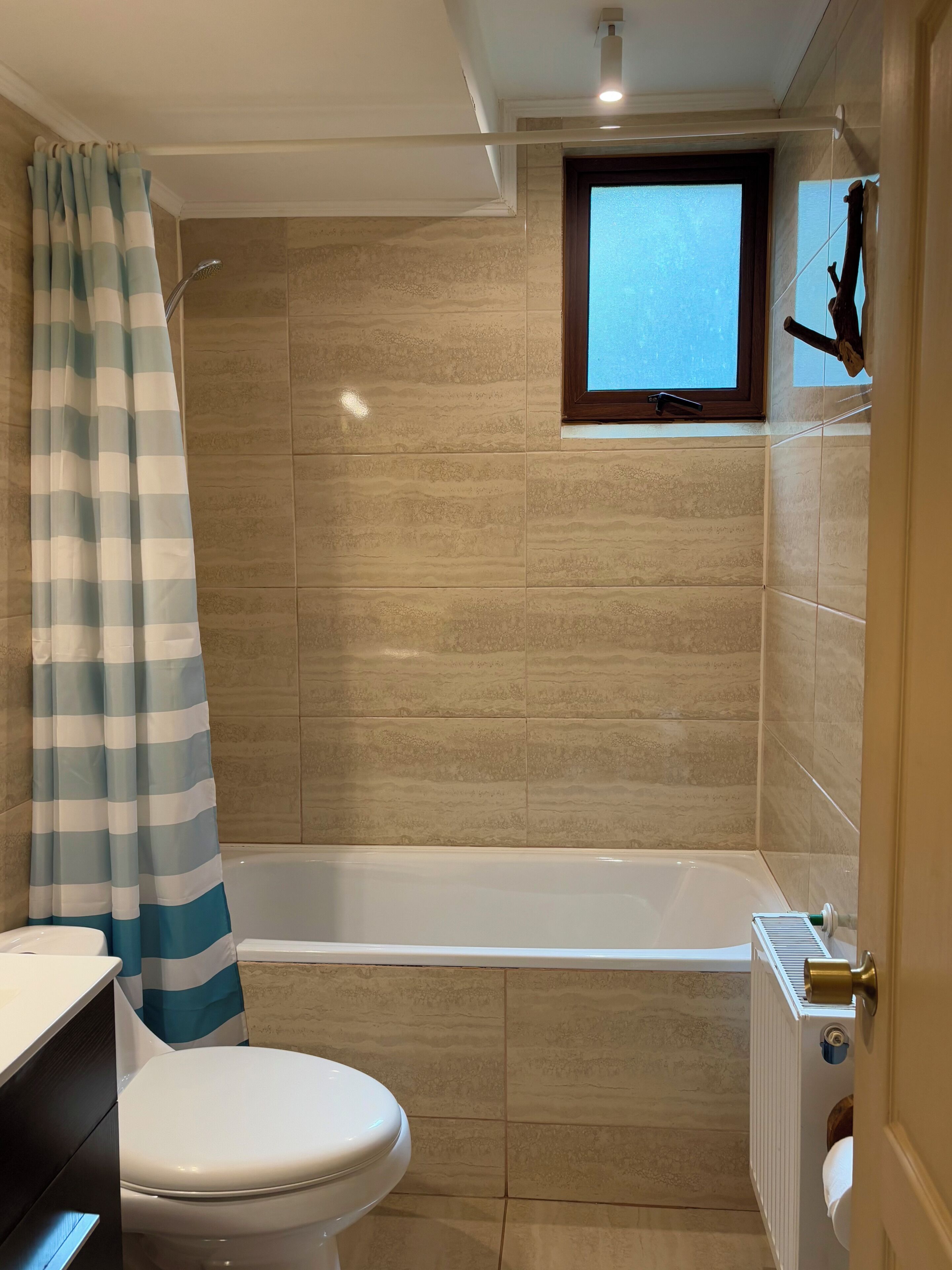 Un baño con bañera, inodoro y una ventana sobre la bañera.