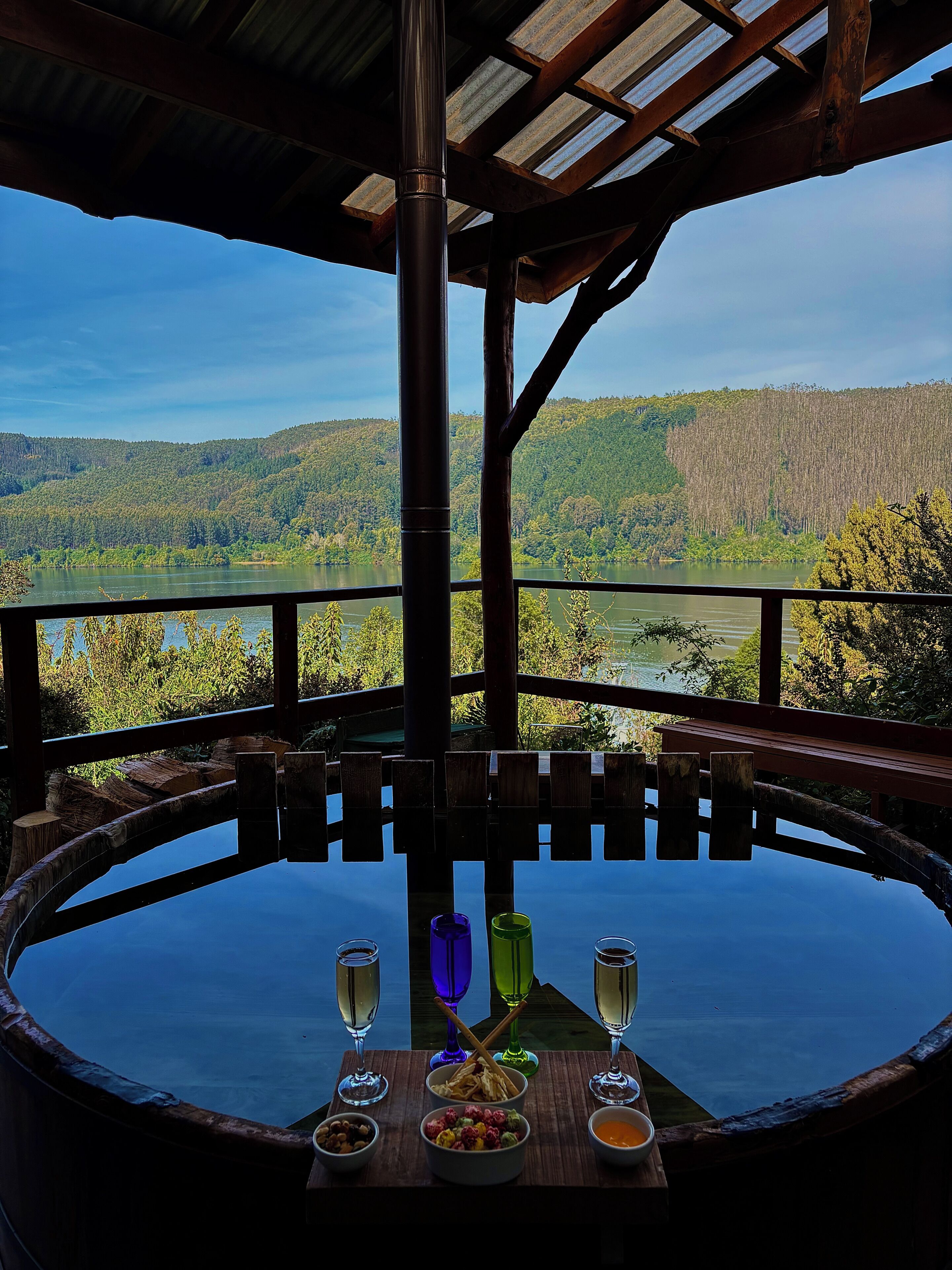 A round table with a view of a lake and forest, surrounded by wooden railings.