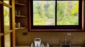 A kitchen with a window view of a forest path, a sink, and a dish rack.