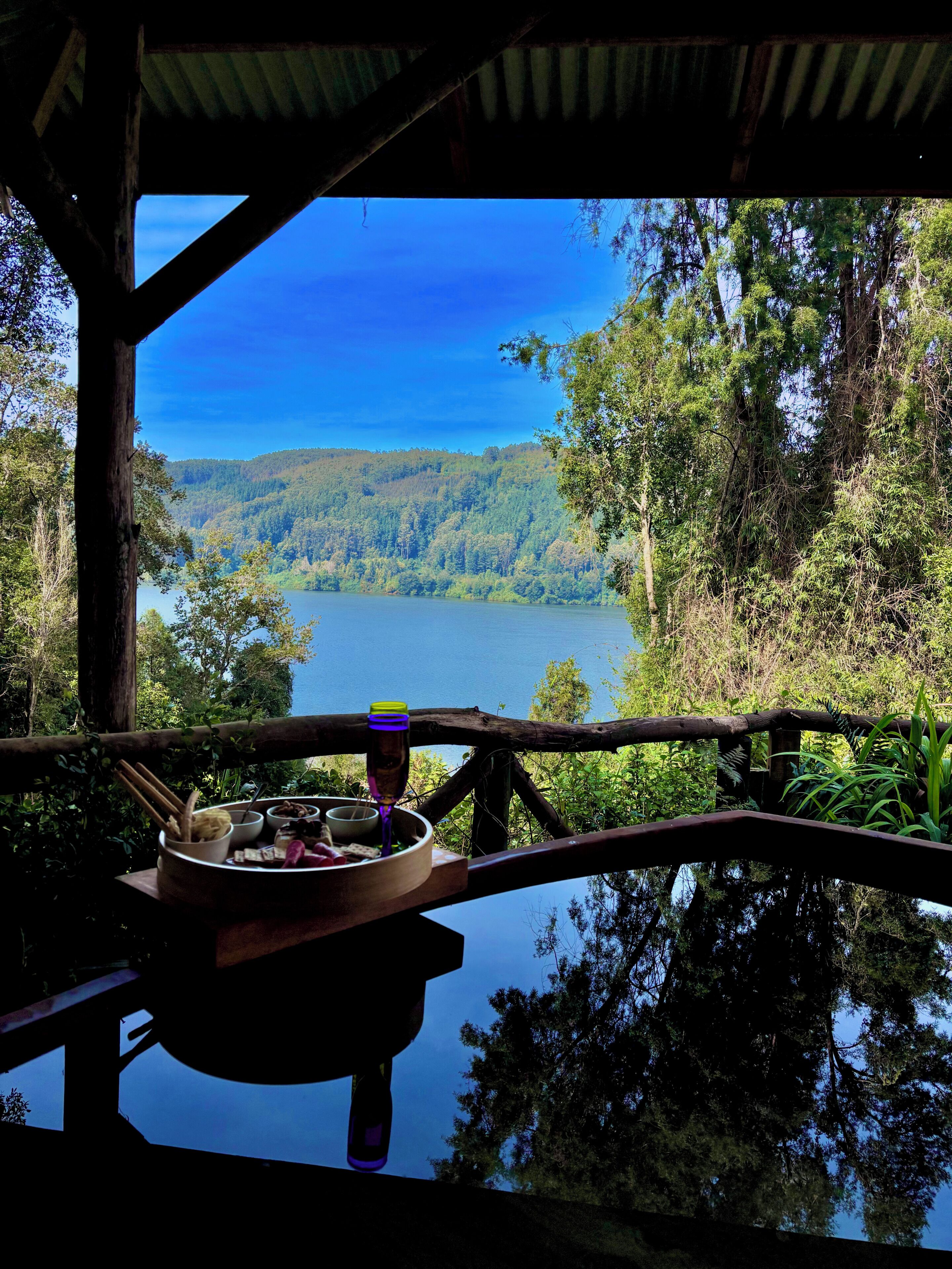 A dining area with a table set for two, overlooking a lake and forested hills.