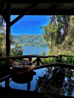 Comedor con una mesa lista para dos personas, con vista a un lago y colinas boscosas.