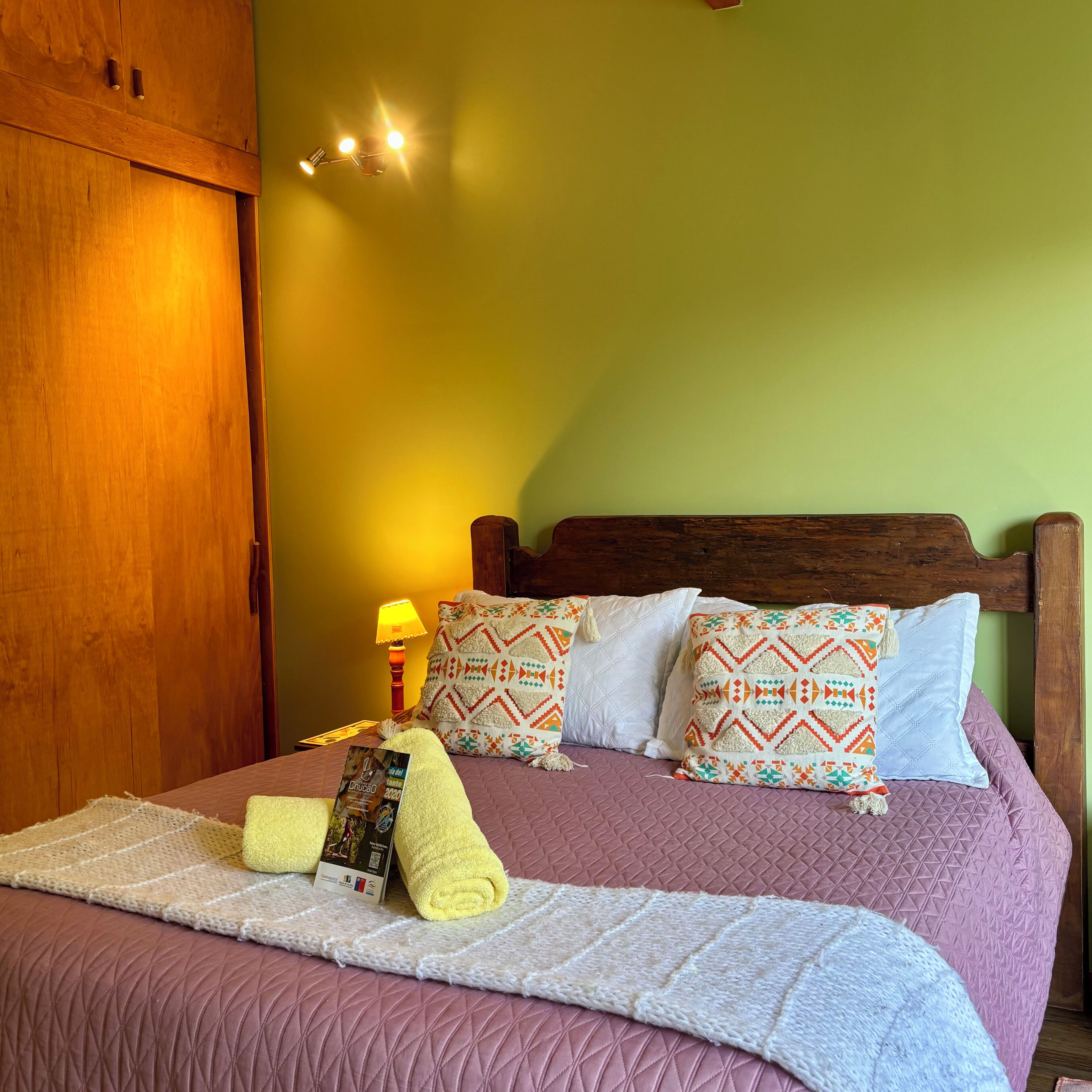 Una cama bien hecha con cabecera acolchada, una lámpara de noche y un cojín decorativo.