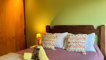 Una cama bien hecha con cabecera acolchada, una lámpara de noche y un cojín decorativo.