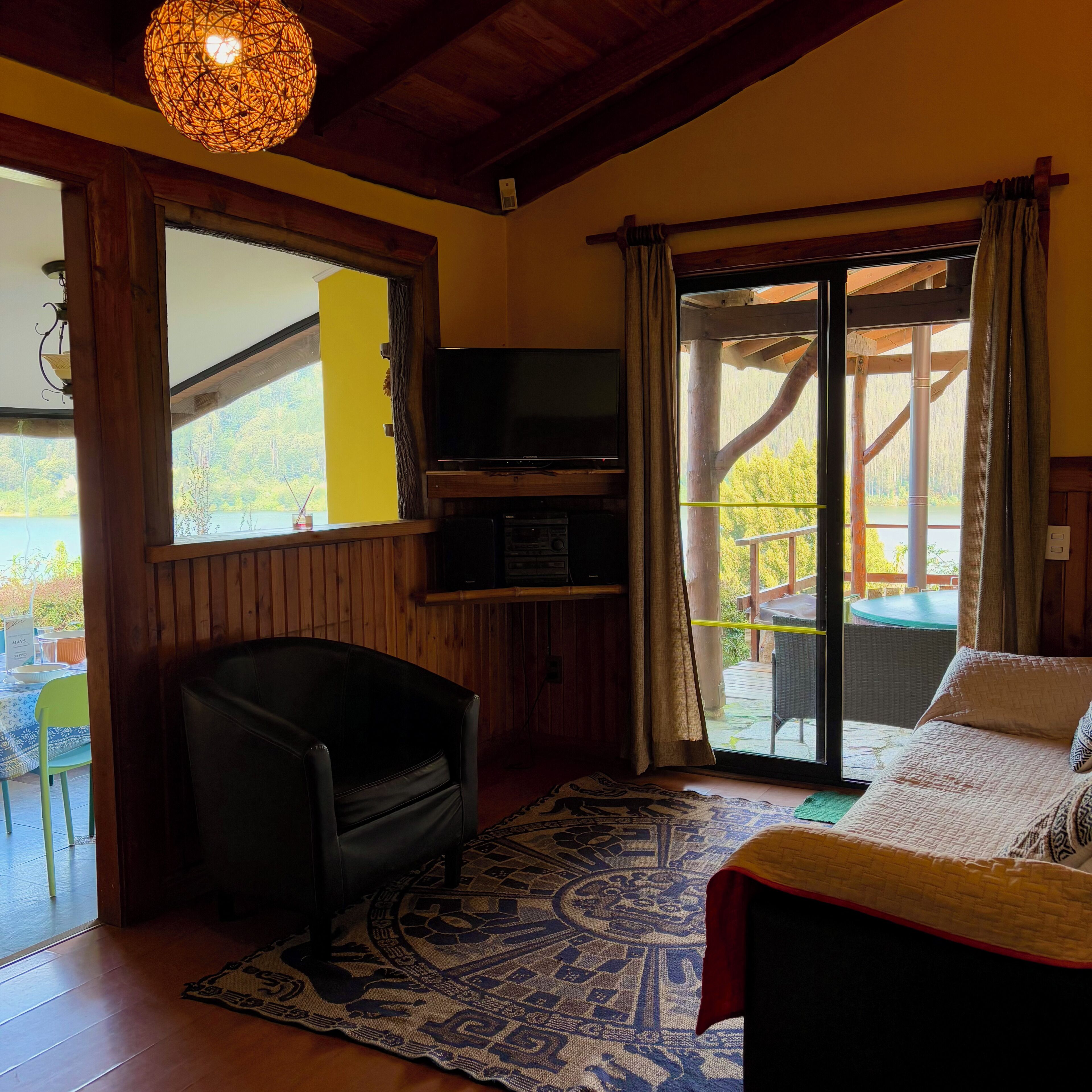 A room with a bed, a television, a chair, and a view of the outdoors.