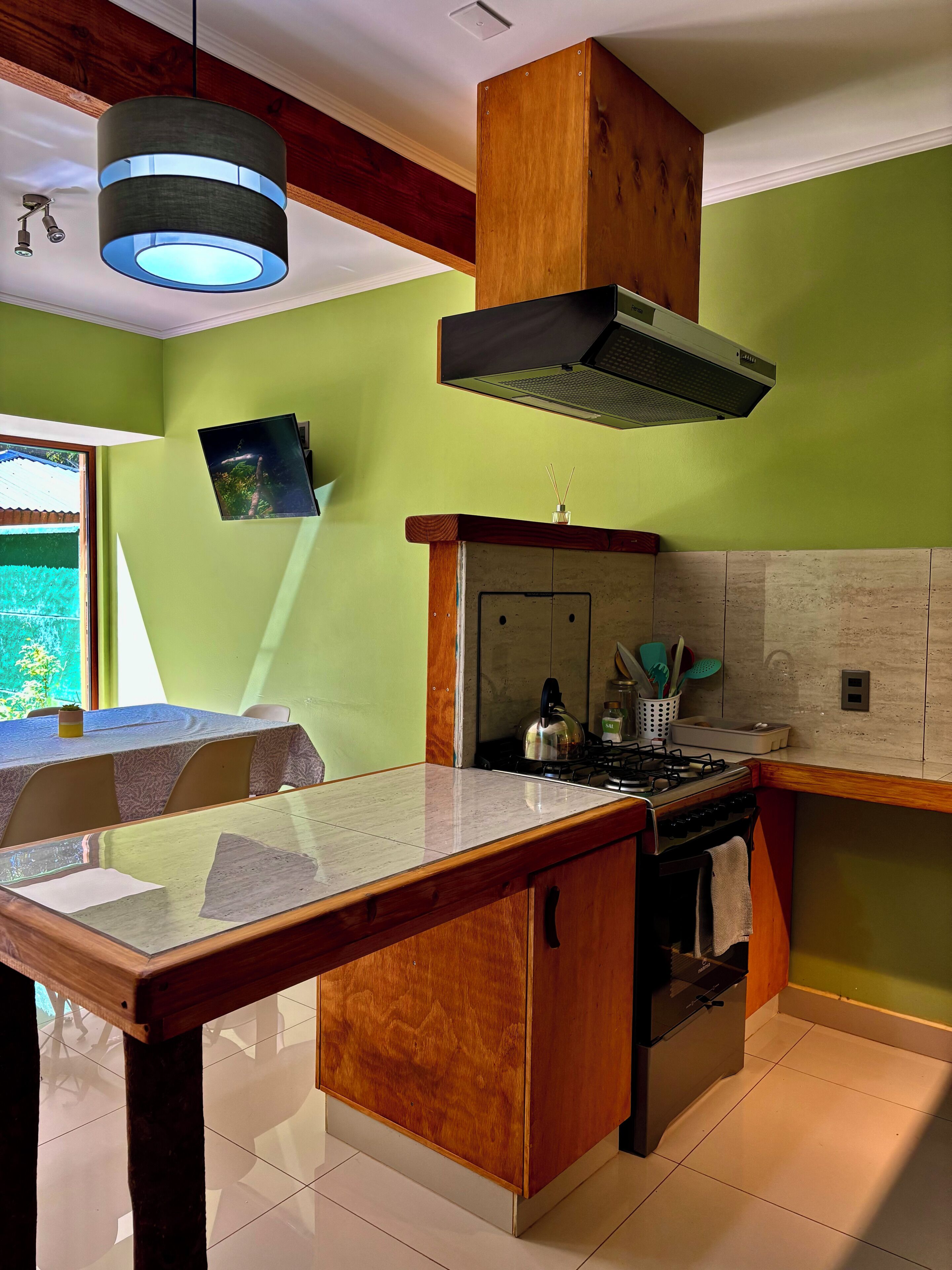 A kitchen with a wooden island, a gas stove, a range hood, and a window with a view of greenery.