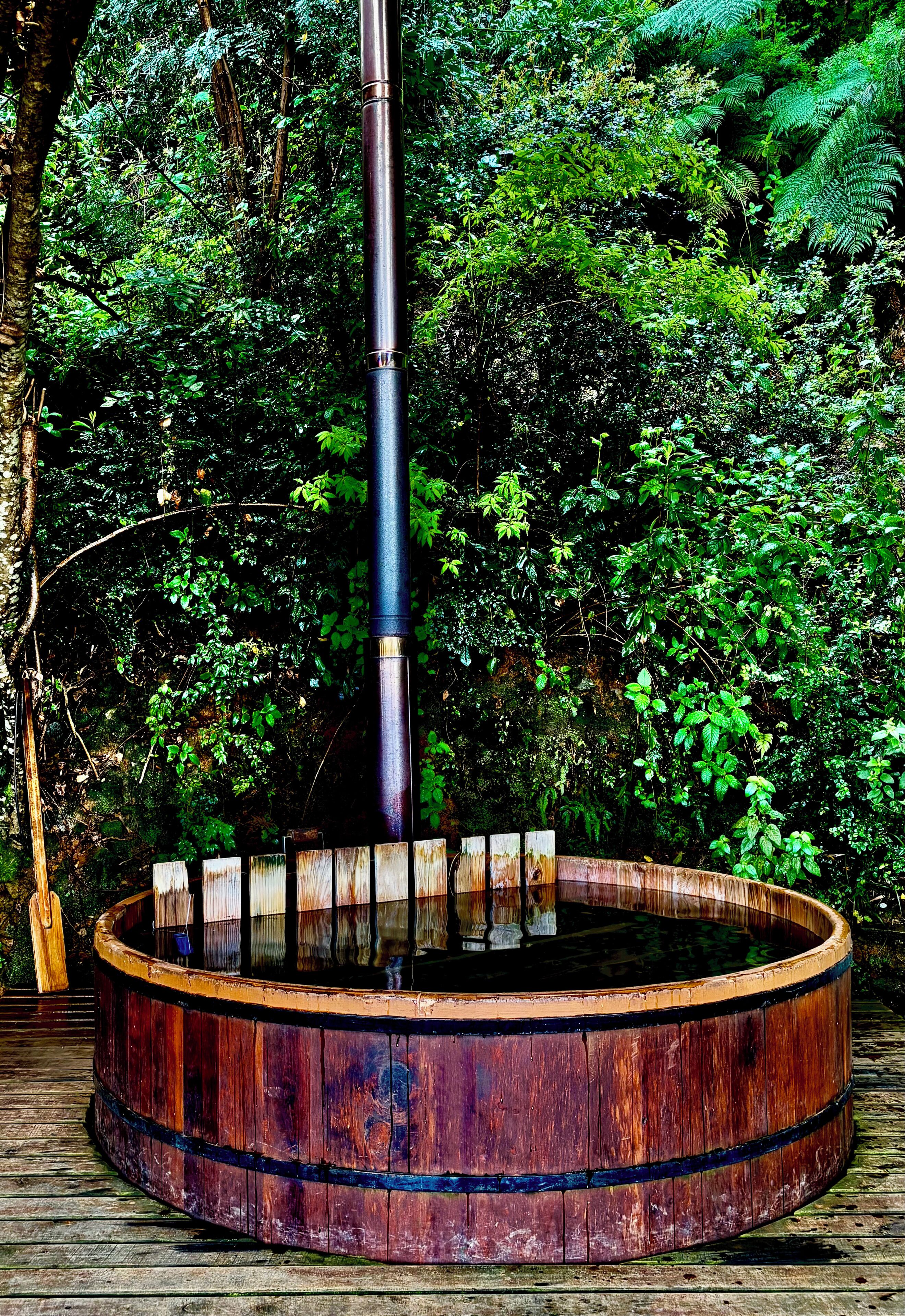 A circular wooden structure with a central pole, surrounded by dense green foliage.