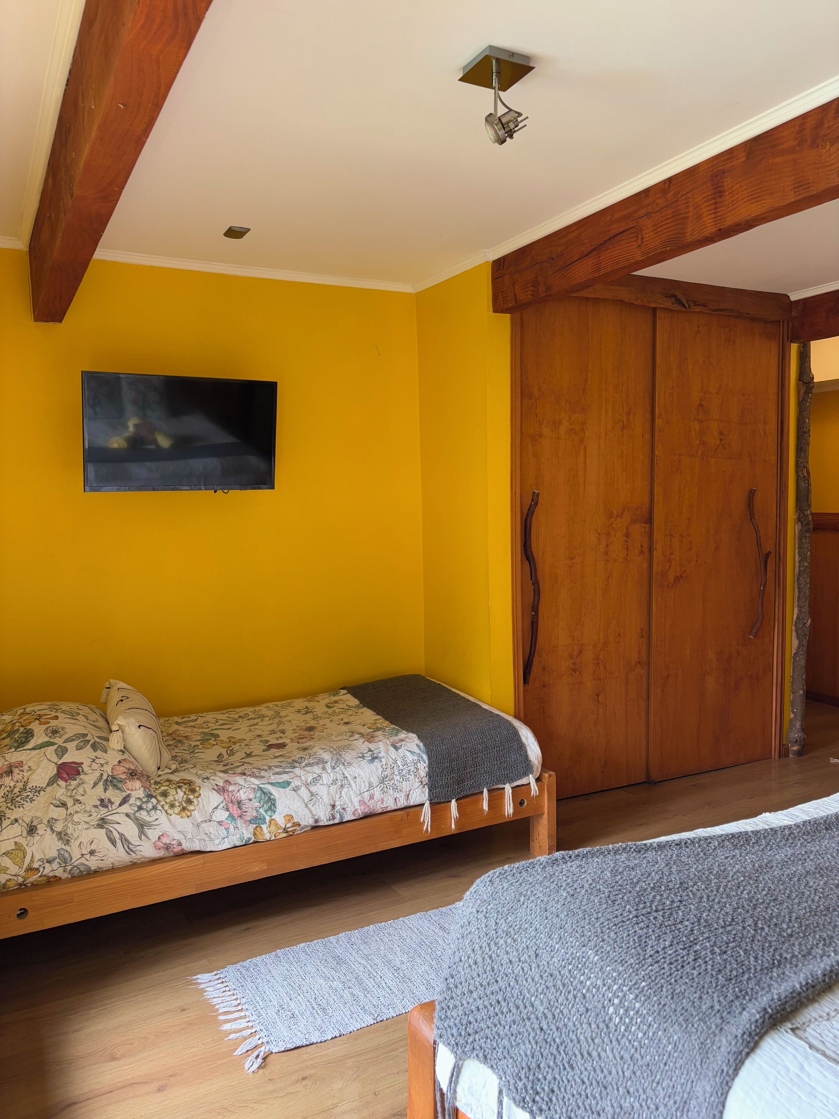 Een kamer met een bed, een houten kledingkast en een televisie aan de muur.