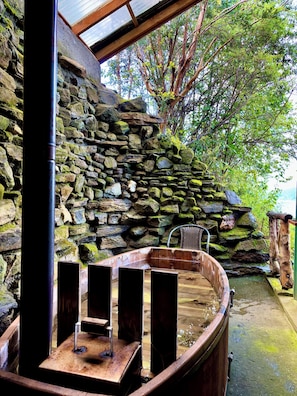 A stone wall, a wooden bench, and a hot tub in an outdoor setting. - Turismo La Rueda del Chucao (Valdivia)