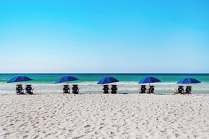 Ein Strand mit fünf blauen Sonnenschirmen und Liegestühlen, die in einer Reihe aufgereiht sind.