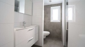 Ein modernes Badezimmer mit einem weißen Waschtisch, einem Spiegel, einer Toilette und einer Duschkabine.