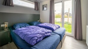 Ein Schlafzimmer mit einem Bett, einem Nachttisch, einem Fenster mit Vorhängen und Blick ins Freie.
