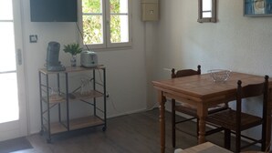 Una habitación con una mesa de comedor de madera, una ventana pequeña con persianas, un televisor montado en la pared y una lámpara en el techo.