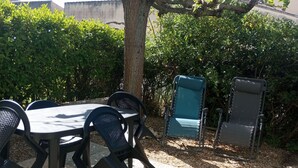 Un patio al aire libre con una mesa y sillas, rodeado de follaje y un árbol.