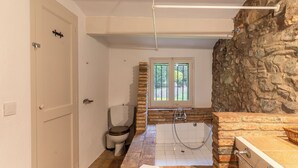 A bathroom with a stone wall, a bathtub, a toilet, and a window. - MOLÍ DE CAN BURJATS (Mont-ras)