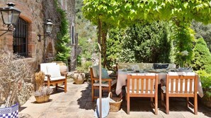 An outdoor patio with a table set for four, surrounded by wooden chairs, a stone building, and greenery. - MOLÍ DE CAN BURJATS (Mont-ras)