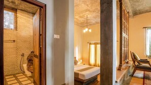 A hotel room with a bed, a bathroom with a shower, and a sitting area with a chair. - Villa Nugaliyadda (CP)