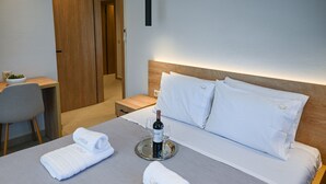 A hotel room with a bed, bedside table, and a chair. There is a bottle of wine and glasses on a tray on the bed. - Estelle luxury living Premium Apartment in Paralia Dionisiou (102) (Paralia Dionisiou)