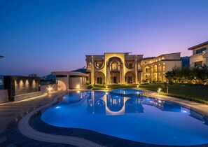 A luxurious pool area with a large, well-lit building in the background. - Oryana Resort (Udaipur)