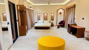 Quarto de hotel moderno com uma cama grande, um banquinho amarelo, uma escrivaninha e uma cadeira.