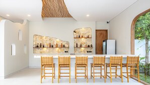 A modern kitchen with a stone backsplash, a white refrigerator, and a bar area with wicker chairs.
