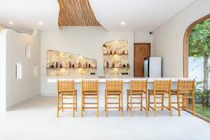 Eine moderne Küche mit Steinrückwand, einem weißen Kühlschrank und einer Bar mit Korbstühlen.