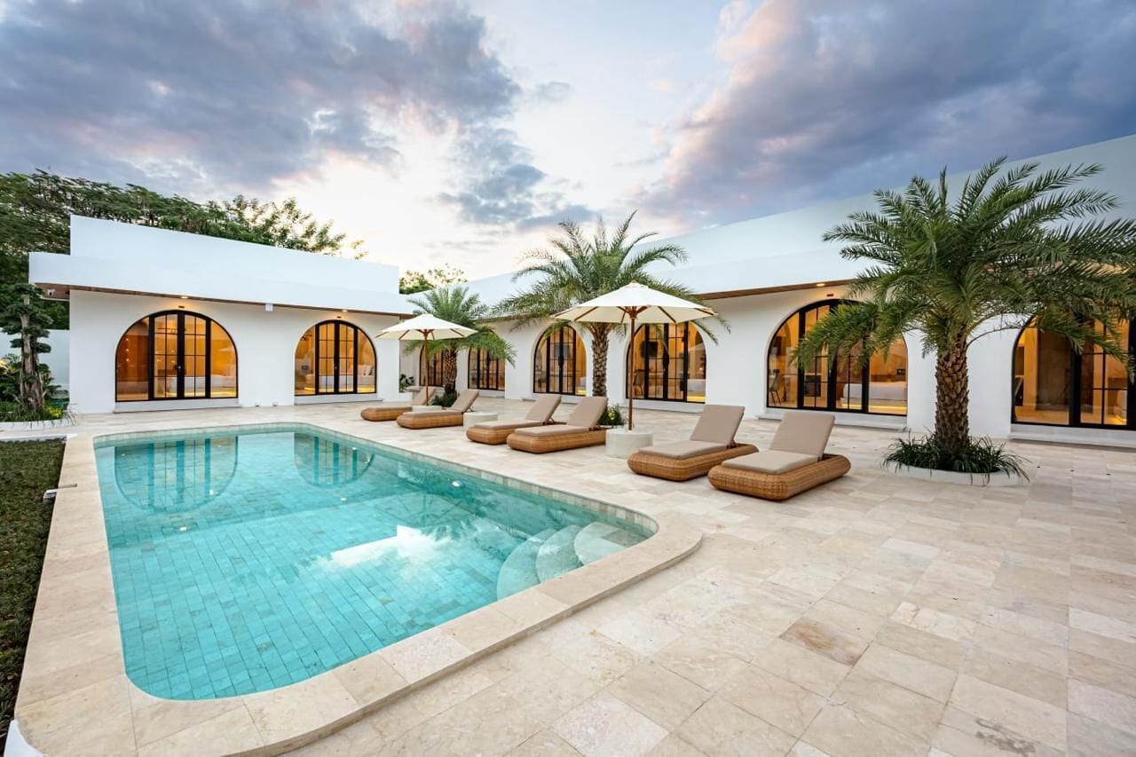 Piscina con sillones de descanso y sombrillas, rodeada por un edificio con ventanales arqueados.
