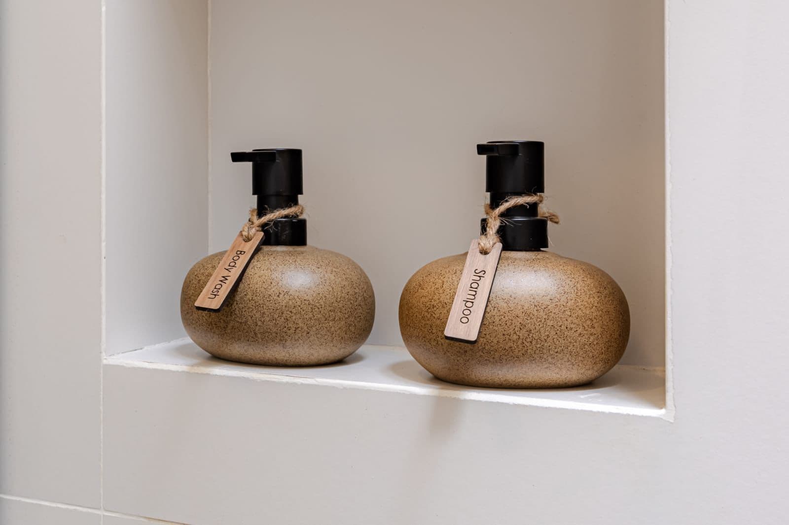 Two spherical containers with black pumps and wooden tags, placed on a white shelf.